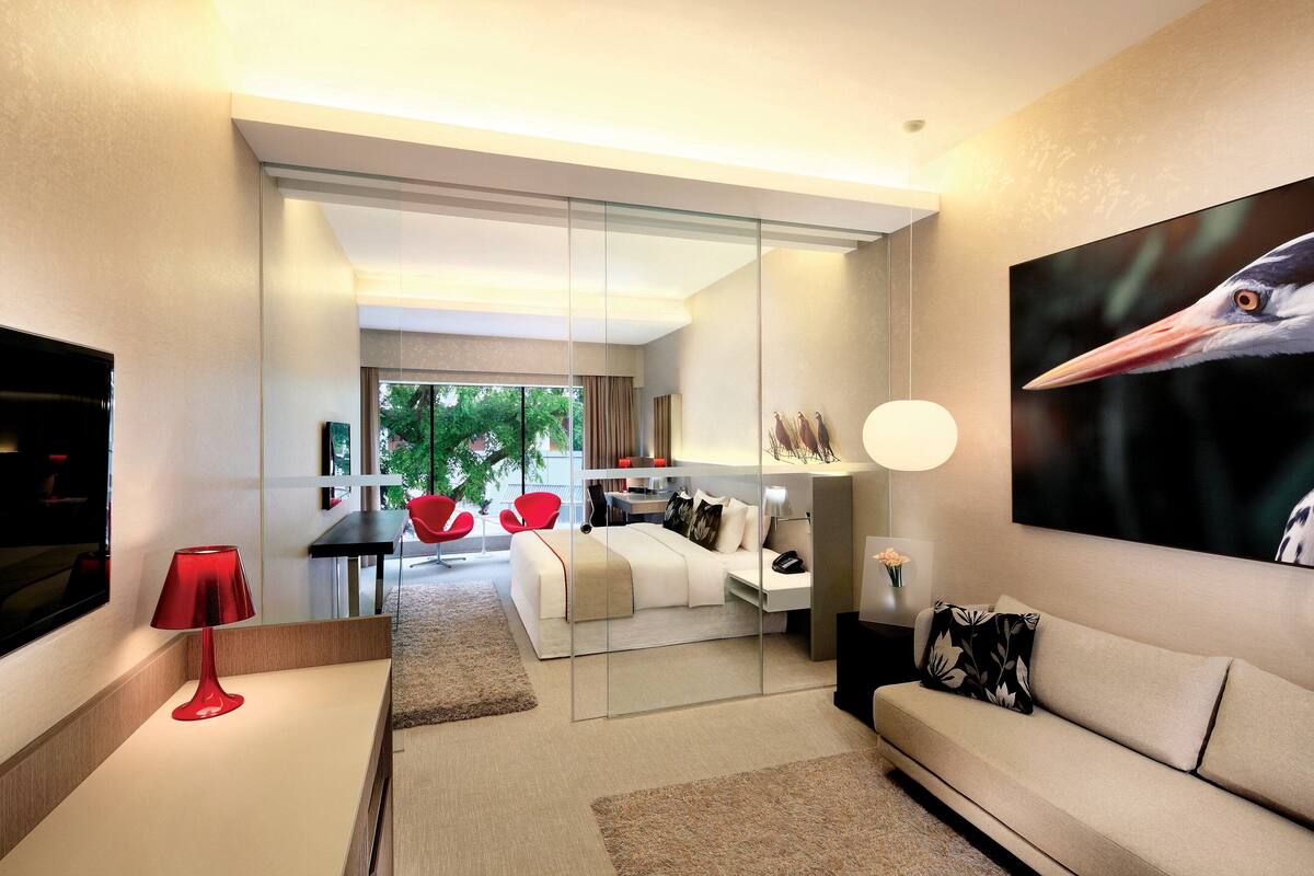 Una sala de estar moderna con un sofá, una lámpara roja, un cuadro grande y un separador de vidrio que da a una zona de comedor con una mesa y sillas.