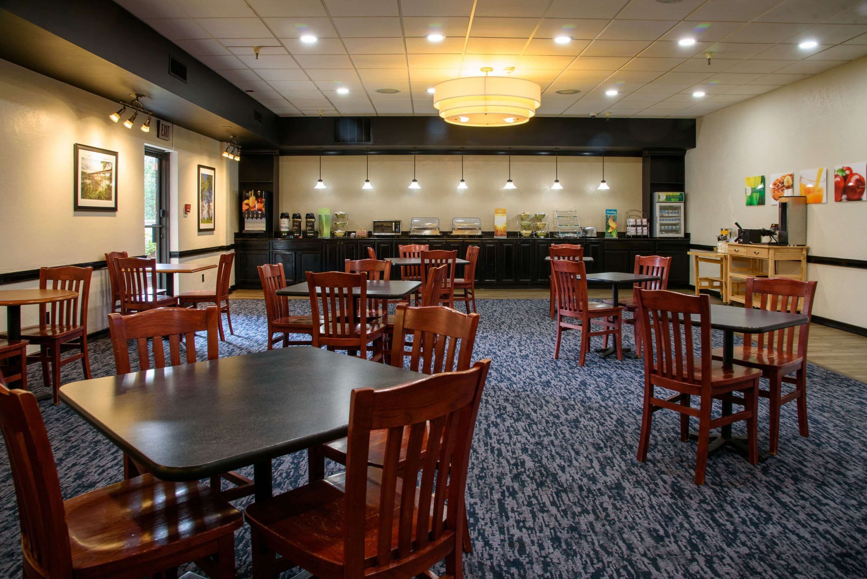 A restaurant with multiple tables and chairs, a counter with a beverage dispenser, and a wall-mounted menu board.