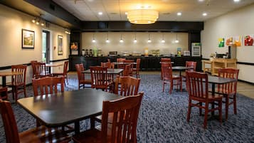 A restaurant with multiple tables and chairs, a counter with a beverage dispenser, and a wall-mounted menu board.