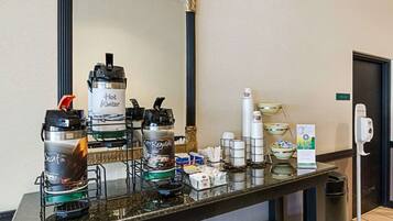 A hotel reception area with a coffee station featuring decaf and regular hot water options, a mirror, and a hand sanitizer dispenser.