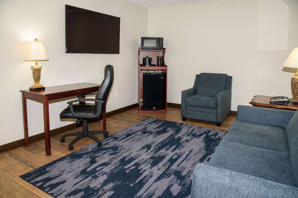 A living room with a desk, two chairs, a television, a coffee maker, and a microwave.