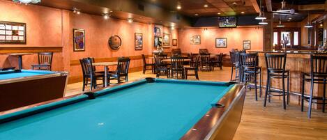 A pool table in a bar area with wooden flooring and multiple seating arrangements.