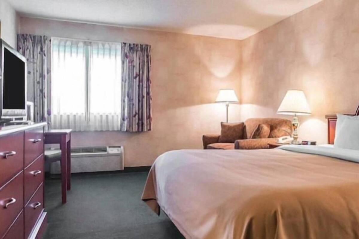 A hotel room with a bed, a desk, a chair, a TV, and a window with curtains.