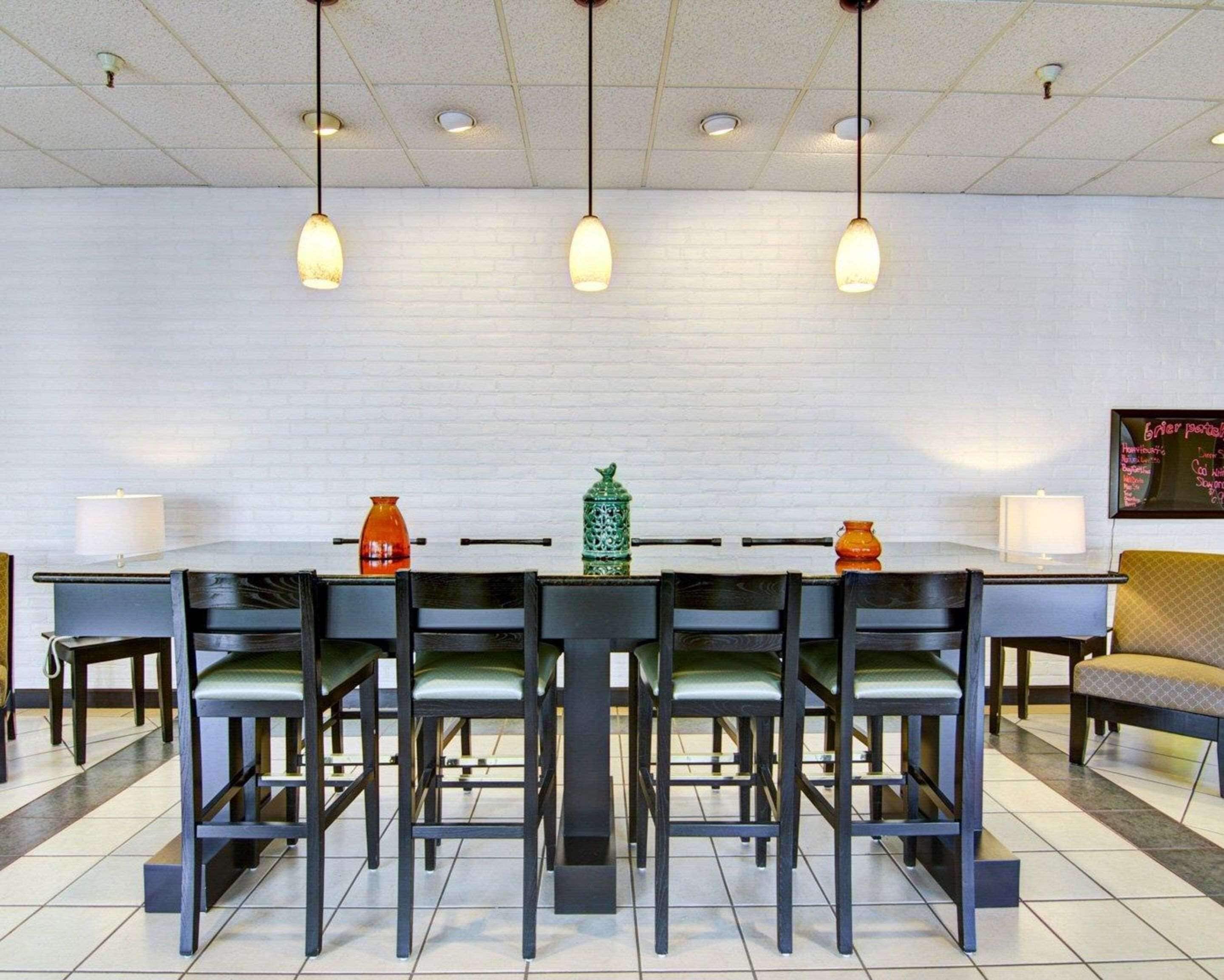 A dining area with a long table, multiple chairs, hanging pendant lights, and decorative vases.