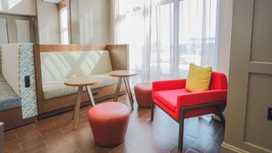 Un interior moderno con un sofá, un reposapiés y una silla roja cerca de ventanas amplias.