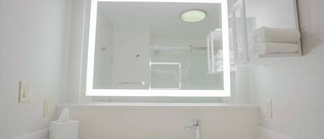 Un baño con un espejo grande, un lavamanos y un perchero para toallas.
