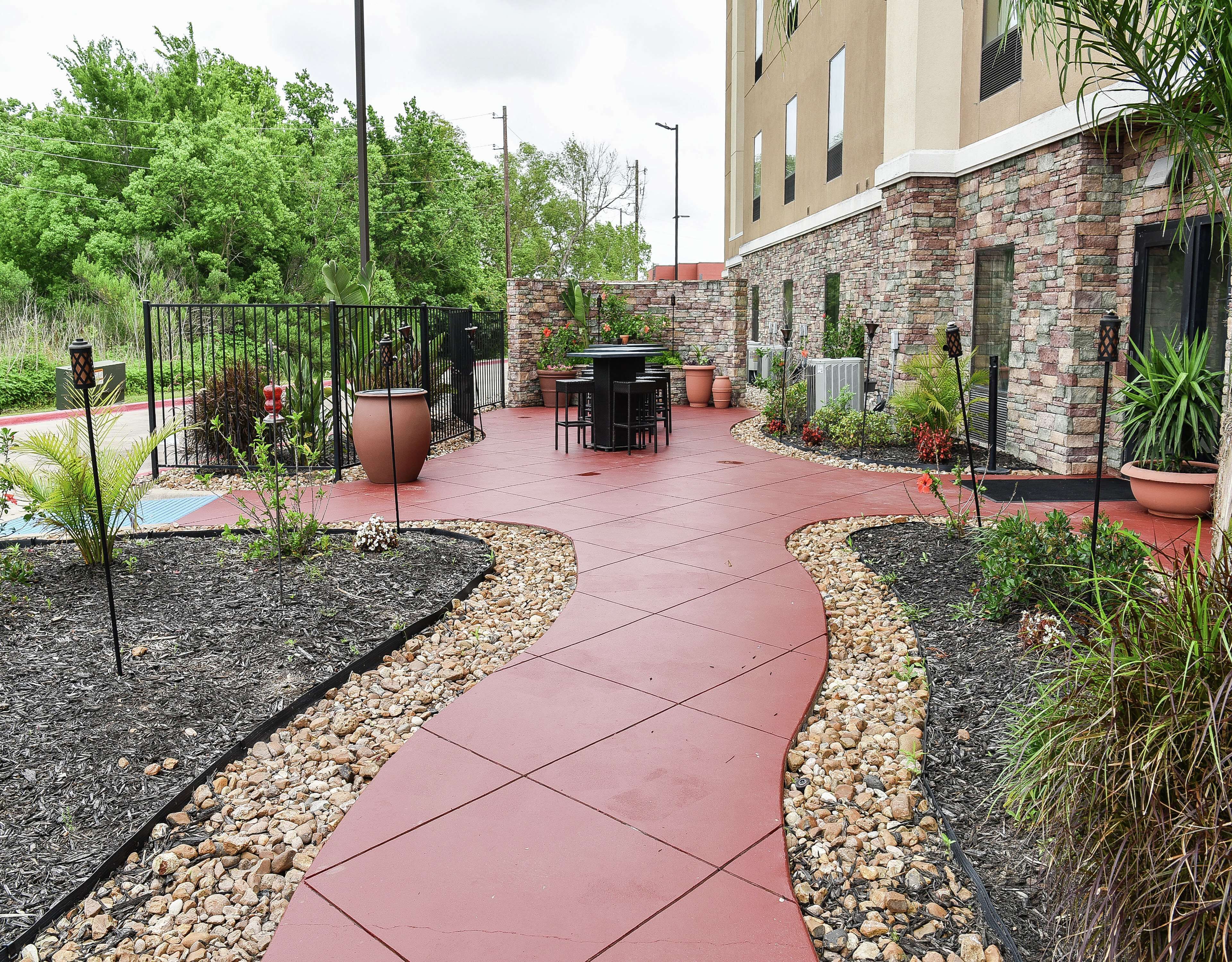 A patio area with a curved red tile walkway, surrounded by potted plants and a stone wall.