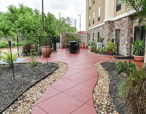 A patio area with a curved red tile walkway, surrounded by potted plants and a stone wall. - Hampton Inn & Suites Bay City, TX (Bay City)