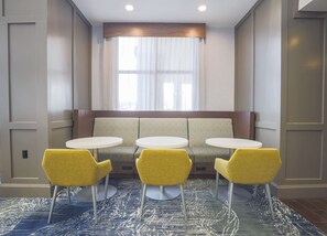 Un espace détente comprenant un canapé et trois tables rondes, chacune accompagnée d’une chaise jaune.