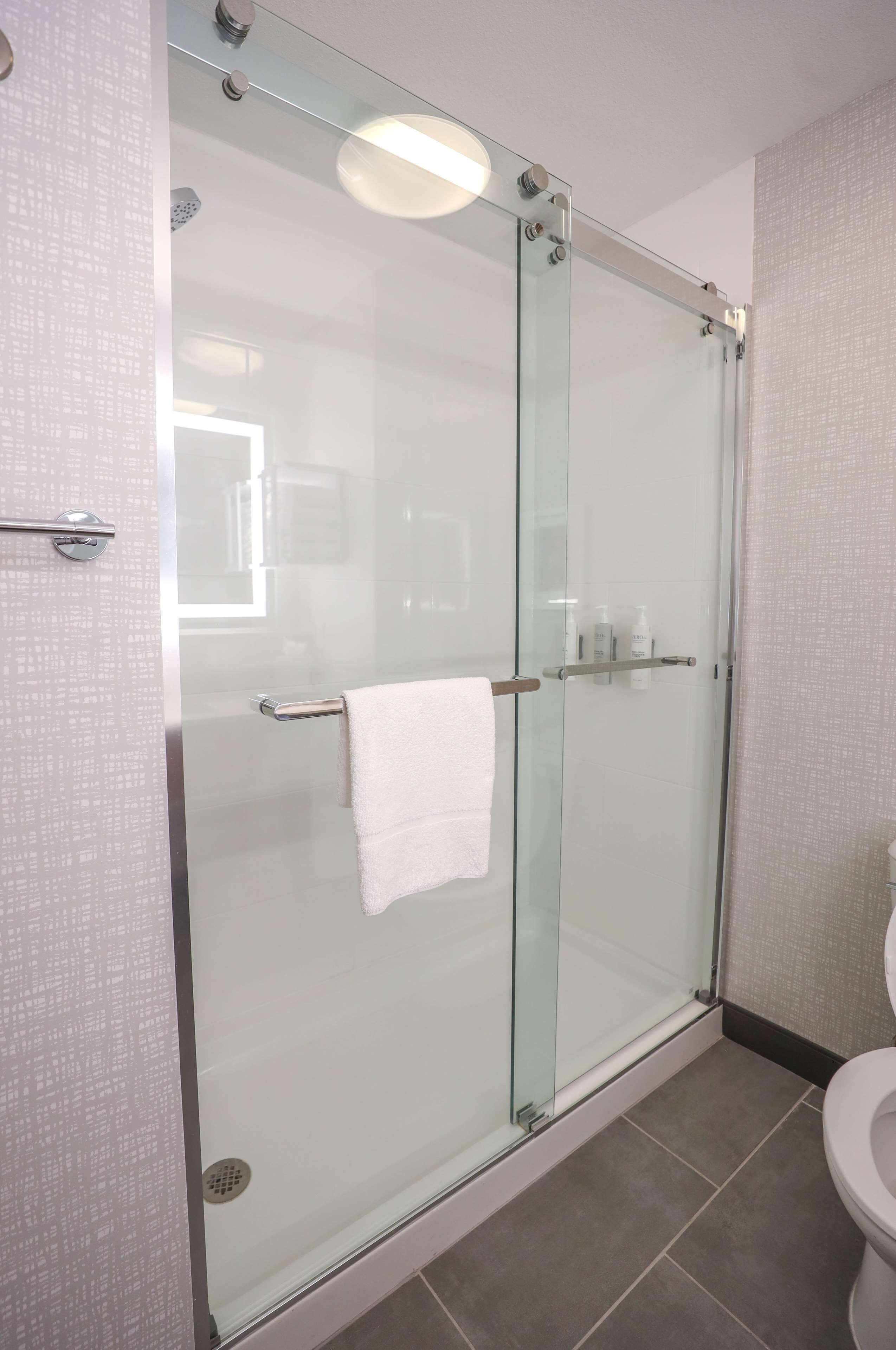 Une salle de bain moderne avec une douche à parois de verre, des toilettes blanches et un porte-serviettes.