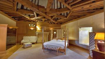 A room with a four-poster bed, a wooden ceiling, a fireplace, and a window with curtains.