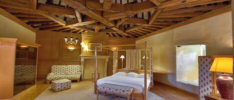 A room with a four-poster bed, a wooden ceiling, a fireplace, and a window with curtains.