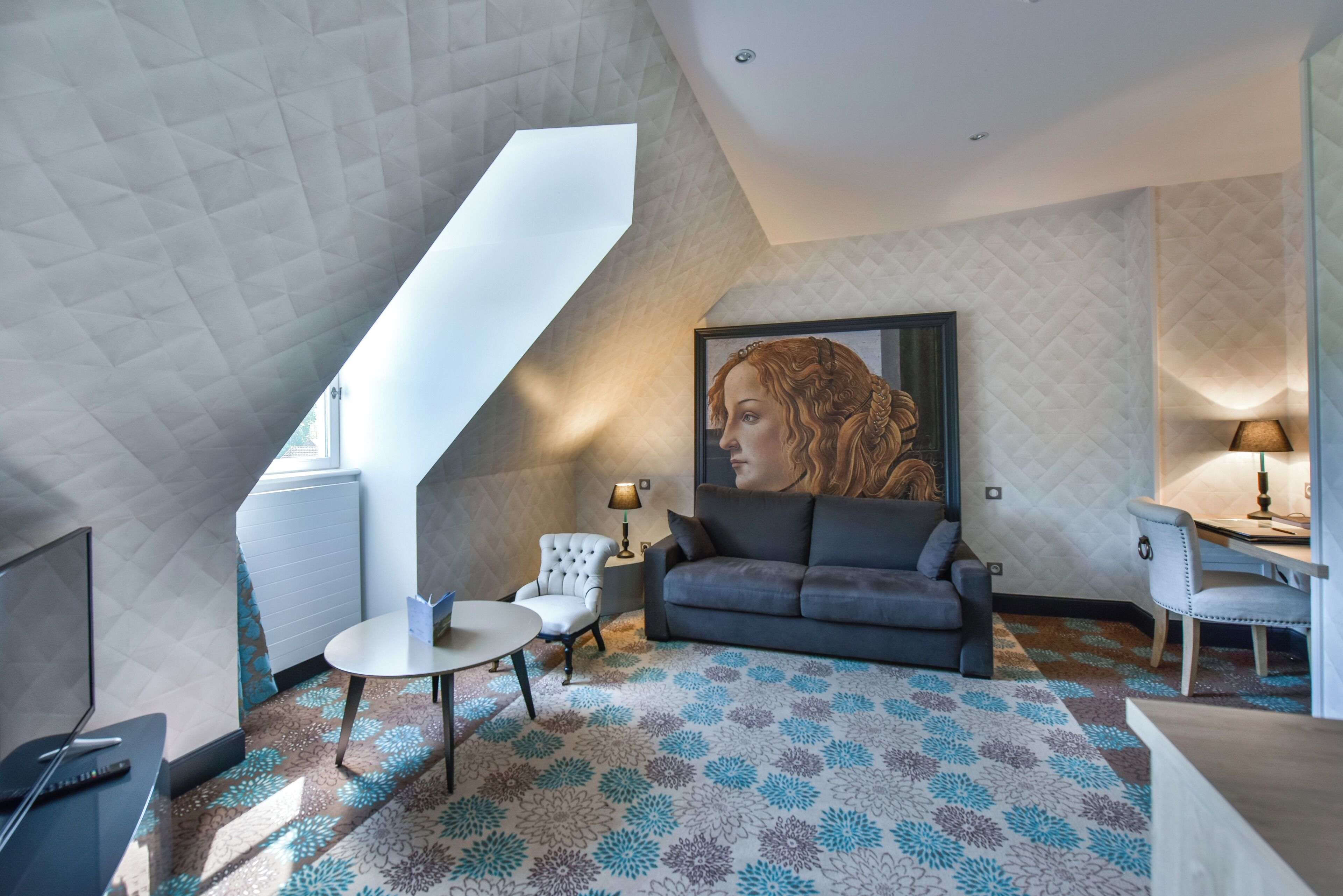 Une chambre de style loft moderne avec un plafond en pente, une grande fenêtre, un canapé, une petite table, une chaise et un tableau.