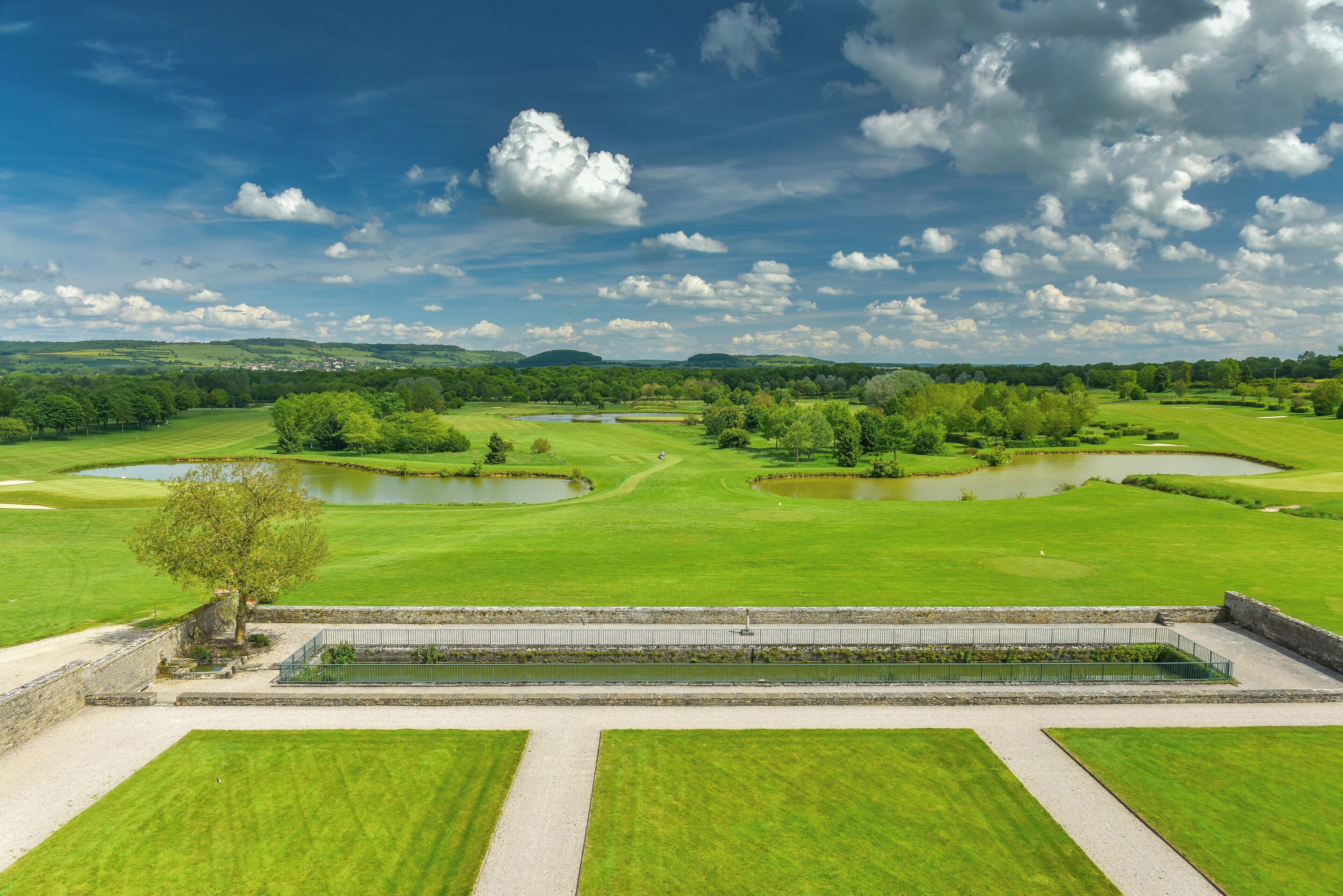 Een golfbaan met meerdere vijvers, een stenen muur en een heldere lucht.