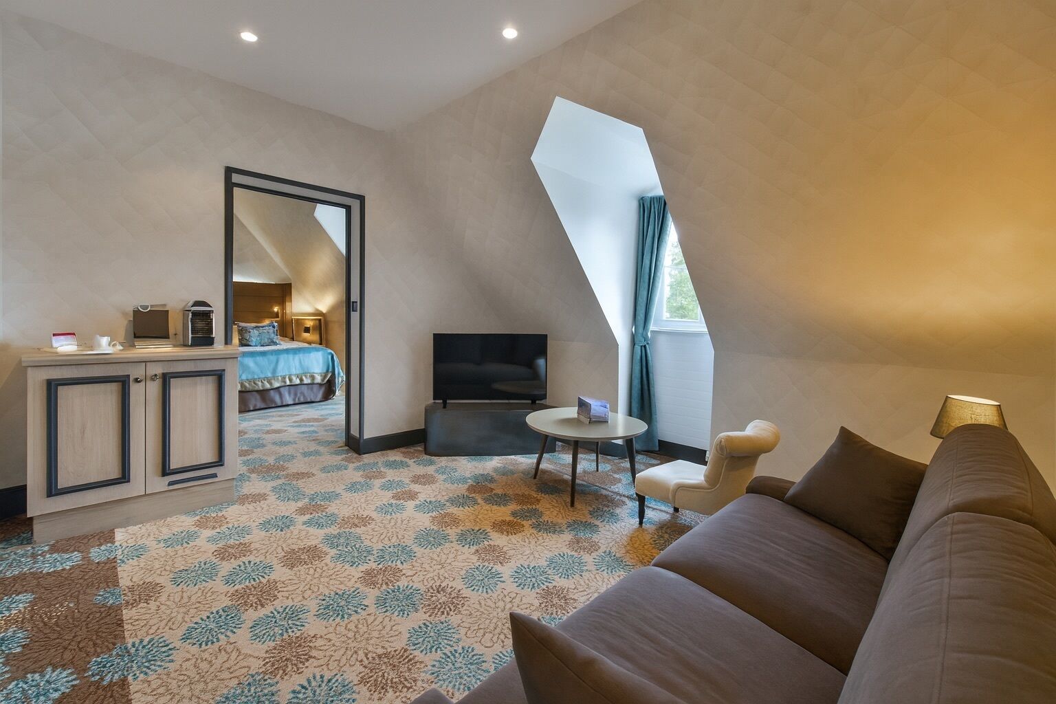 A modern hotel room with a large bed, a TV, a desk, and a sofa.