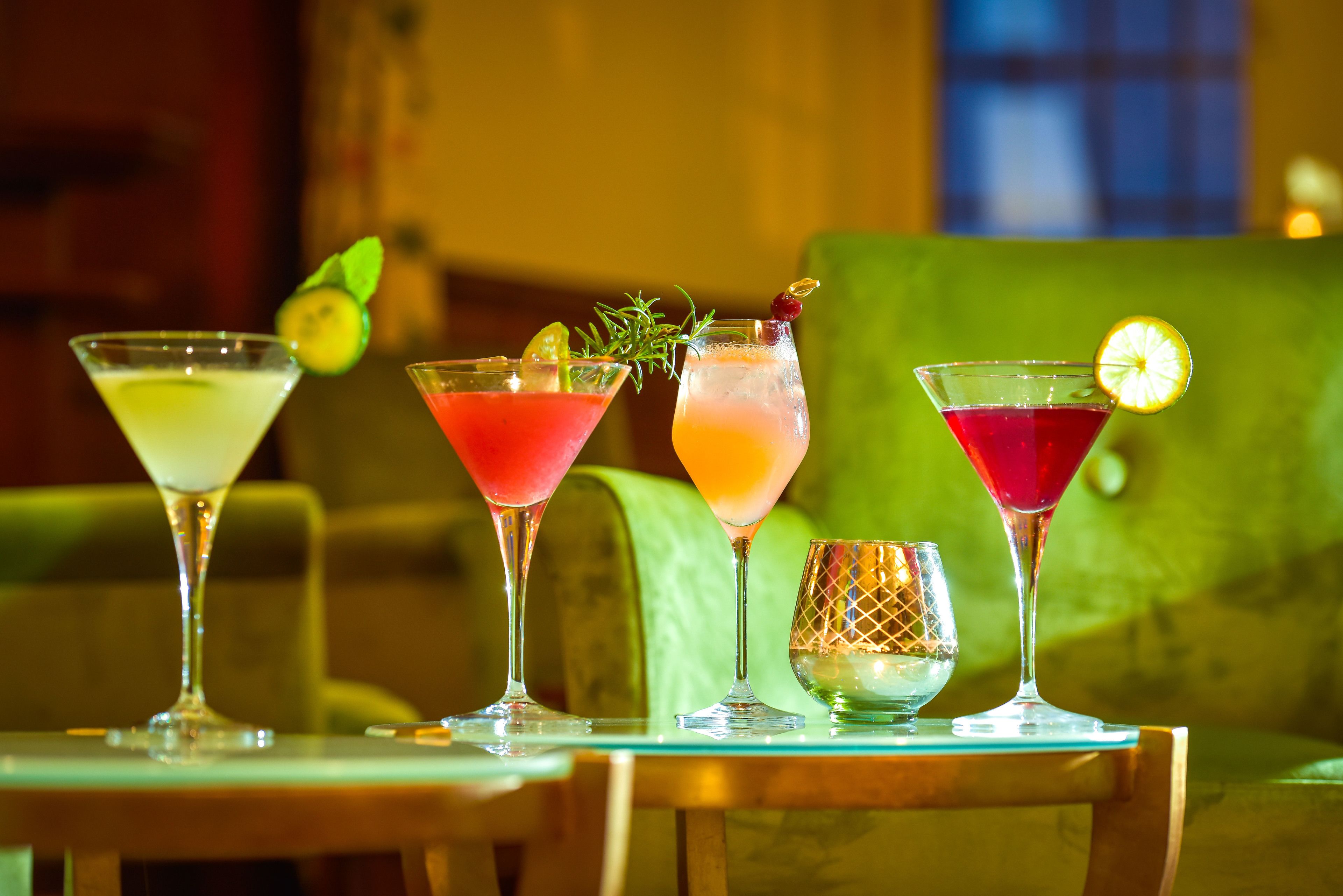 Four cocktails on a table with a green couch in the background.