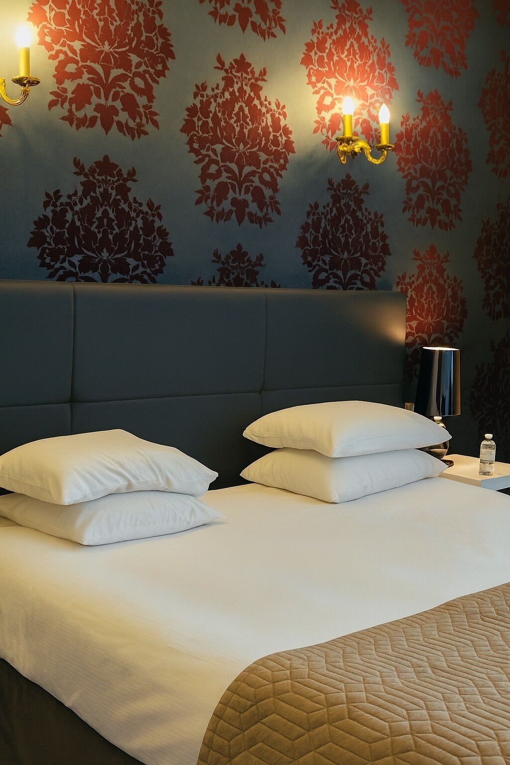 Una cama con ropa blanca y dos almohadas, un cabecero y una pared con estampado floral.