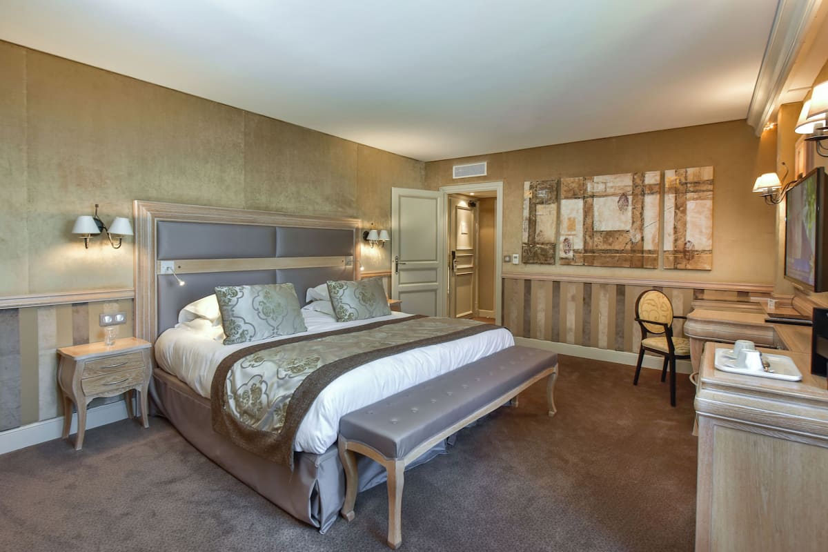A bedroom with a large bed, bedside tables, a bench, a chair, and a desk with a lamp.