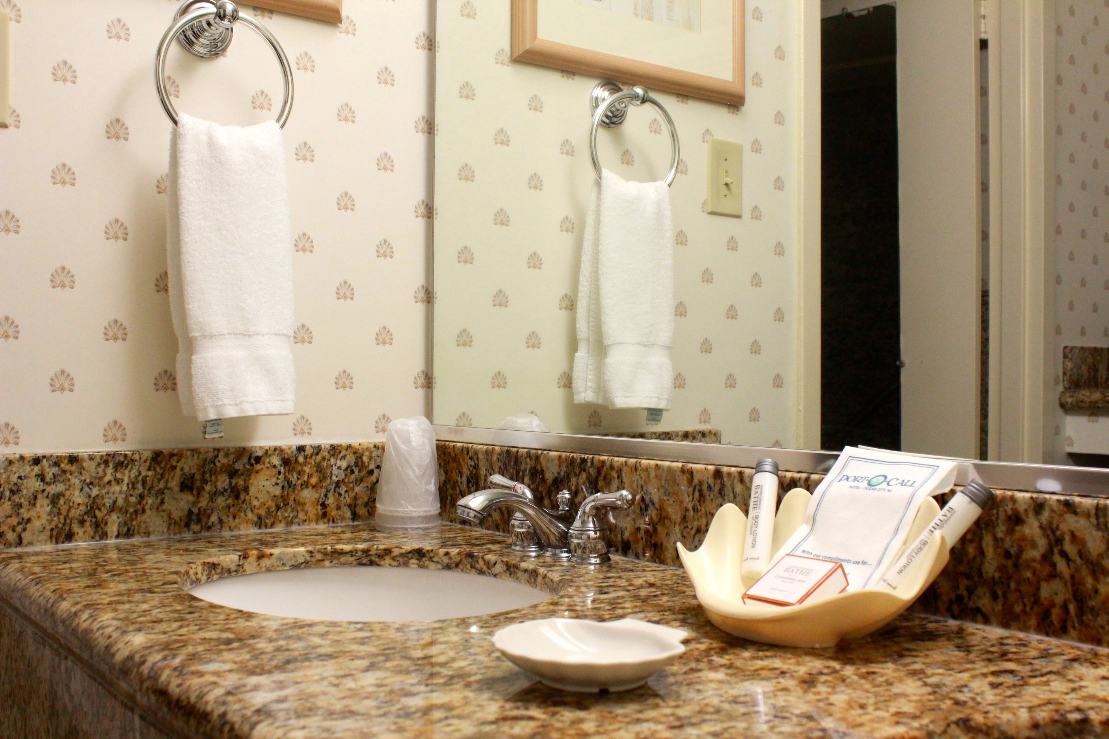 A bathroom with a granite countertop, a sink, a mirror, and two towels hanging on towel rings.