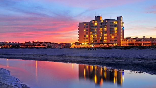 A beachfront hotel with multiple floors, balconies, and a reflection in the calm water. - Port-O-Call Hotel (Ocean City)