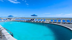 A pool with blue chairs and umbrellas, surrounded by a fence. - Port-O-Call Hotel (Ocean City)