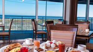 A breakfast table with various dishes, a view of the ocean, and a balcony with chairs. - Port-O-Call Hotel (Ocean City)