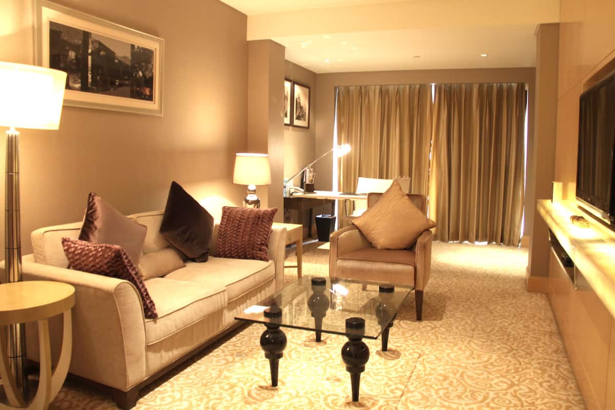 A hotel room with a sofa, armchair, and a glass coffee table.