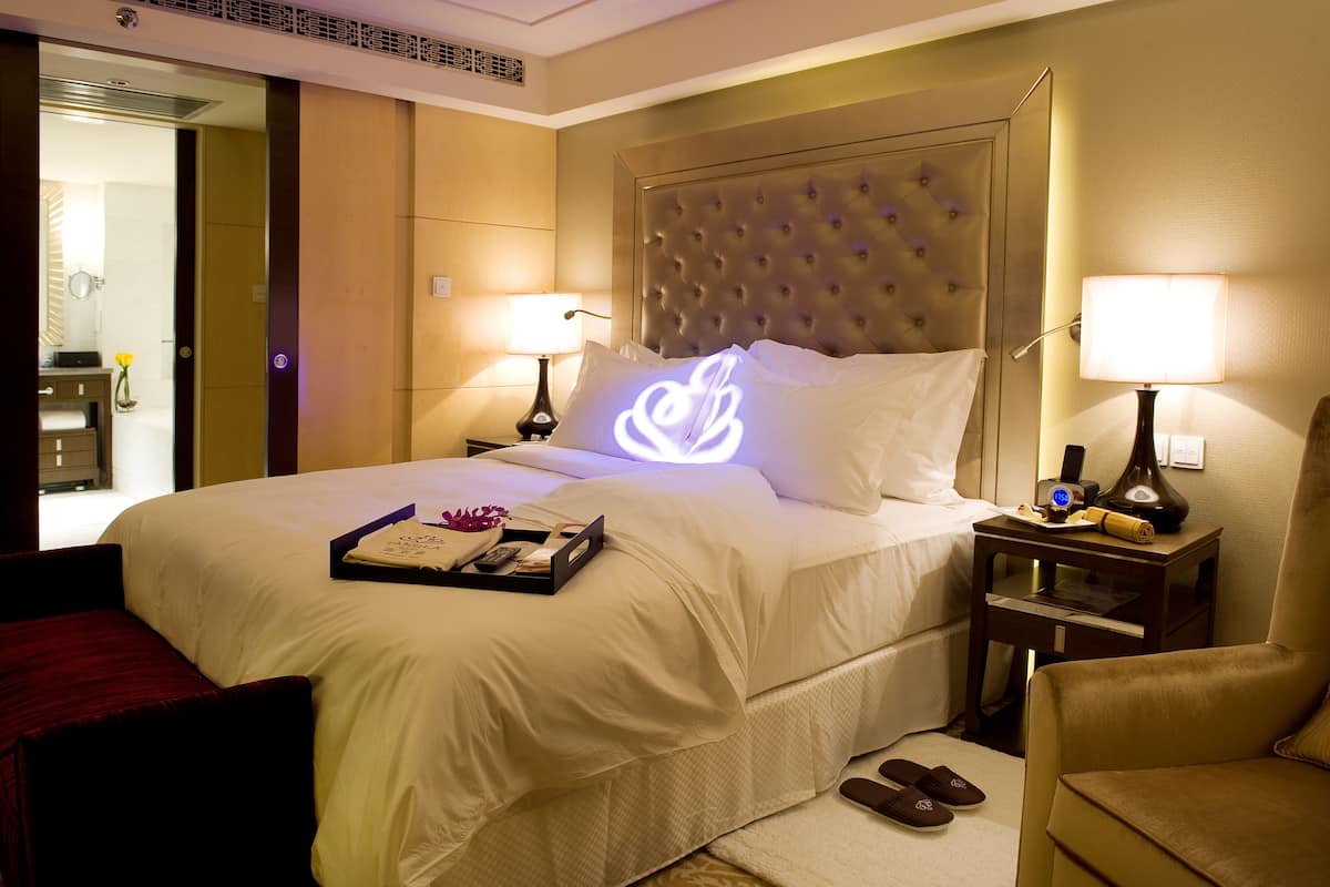 A hotel room with a large bed, two bedside tables, a chair, and a bathroom visible through an open door.