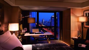 Habitación de hotel con vista a la ciudad, un escritorio, una silla, una cama y una lámpara.