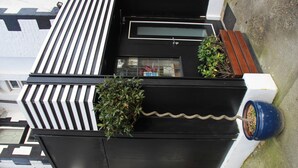 A black and white building with a window, a door, and a small garden area with a potted plant. - The Firs Lodge (Hounslow)