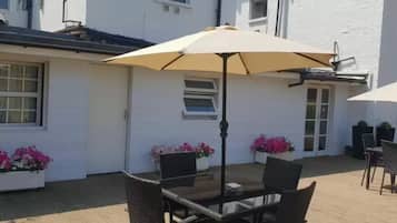 An outdoor patio with a table and chairs, a beige umbrella, and potted plants.