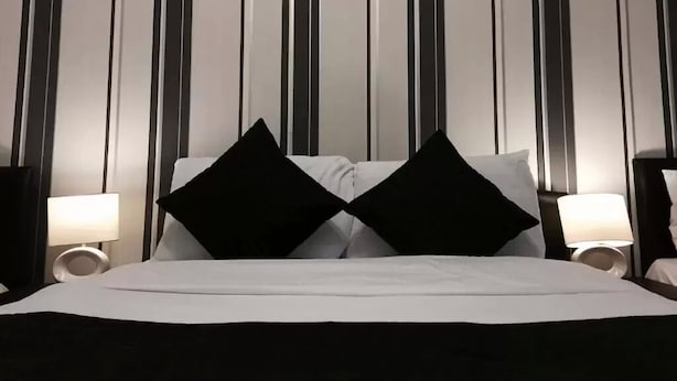 A hotel room with a bed, two black pillows, and two bedside lamps. - The Firs Lodge (Hounslow)