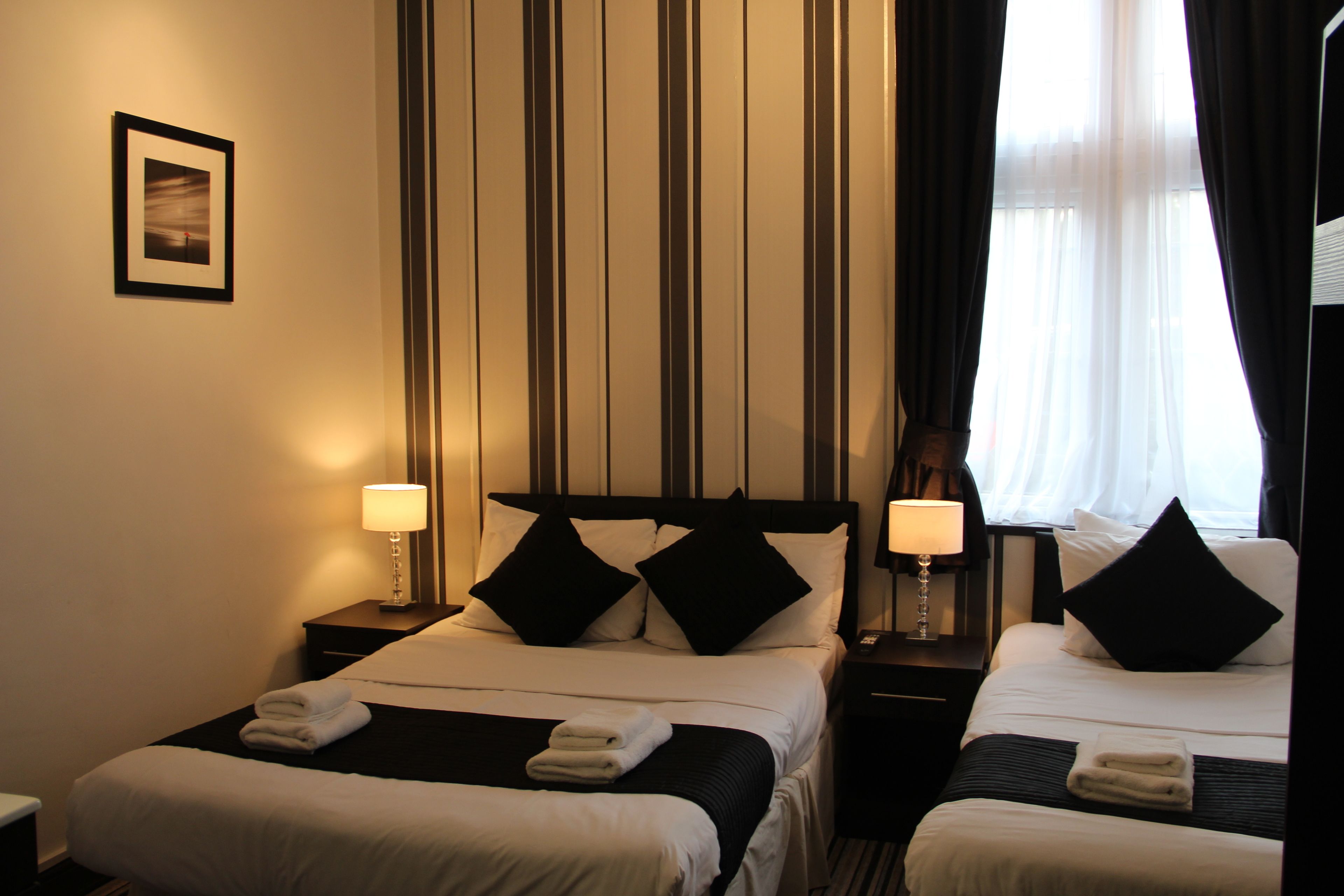 Habitación de hotel con dos camas, cada una con cabecero a rayas blanco y negro, ropa de cama blanca y una mesita de noche pequeña con lámpara.
