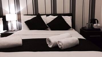 Een keurig opgemaakt bed met zwart-wit beddengoed, een opgevouwen handdoek en een nachtkastje met een lamp en een klein object.