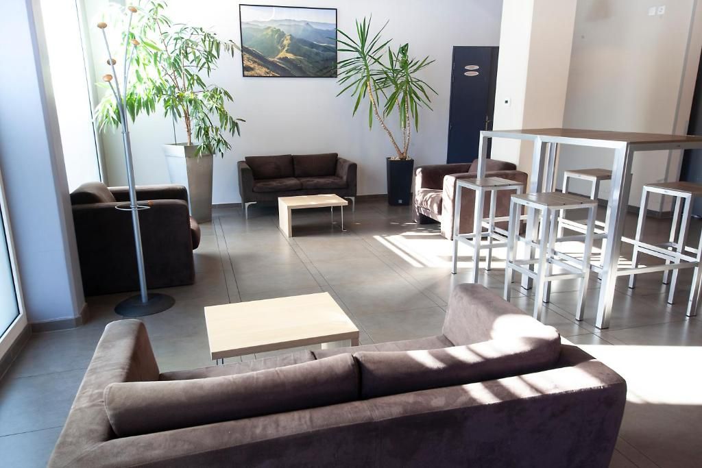 Una sala de estar moderna con sofá, mesa de centro y comedor con sillas. Hay plantas en macetas y un cuadro en la pared.