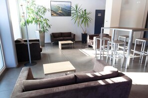 Ein modernes Wohnzimmer mit einer Couch, einem Couchtisch und einem Essbereich mit Stühlen. Üchtopf-Pflanzen und ein Gemälde zieren die Wand.