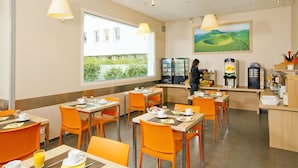 A modern dining area with orange chairs and tables, a coffee machine, and a view of greenery outside. - Residhome Clermont Ferrand Gergovia (Clermont-Ferrand)