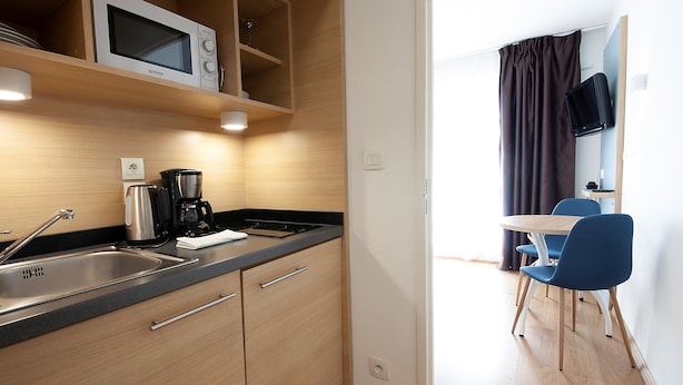 A compact kitchen with a microwave, coffee maker, and a sink. There is a dining area with a table and chairs. - Residhome Clermont Ferrand Gergovia (Clermont-Ferrand)