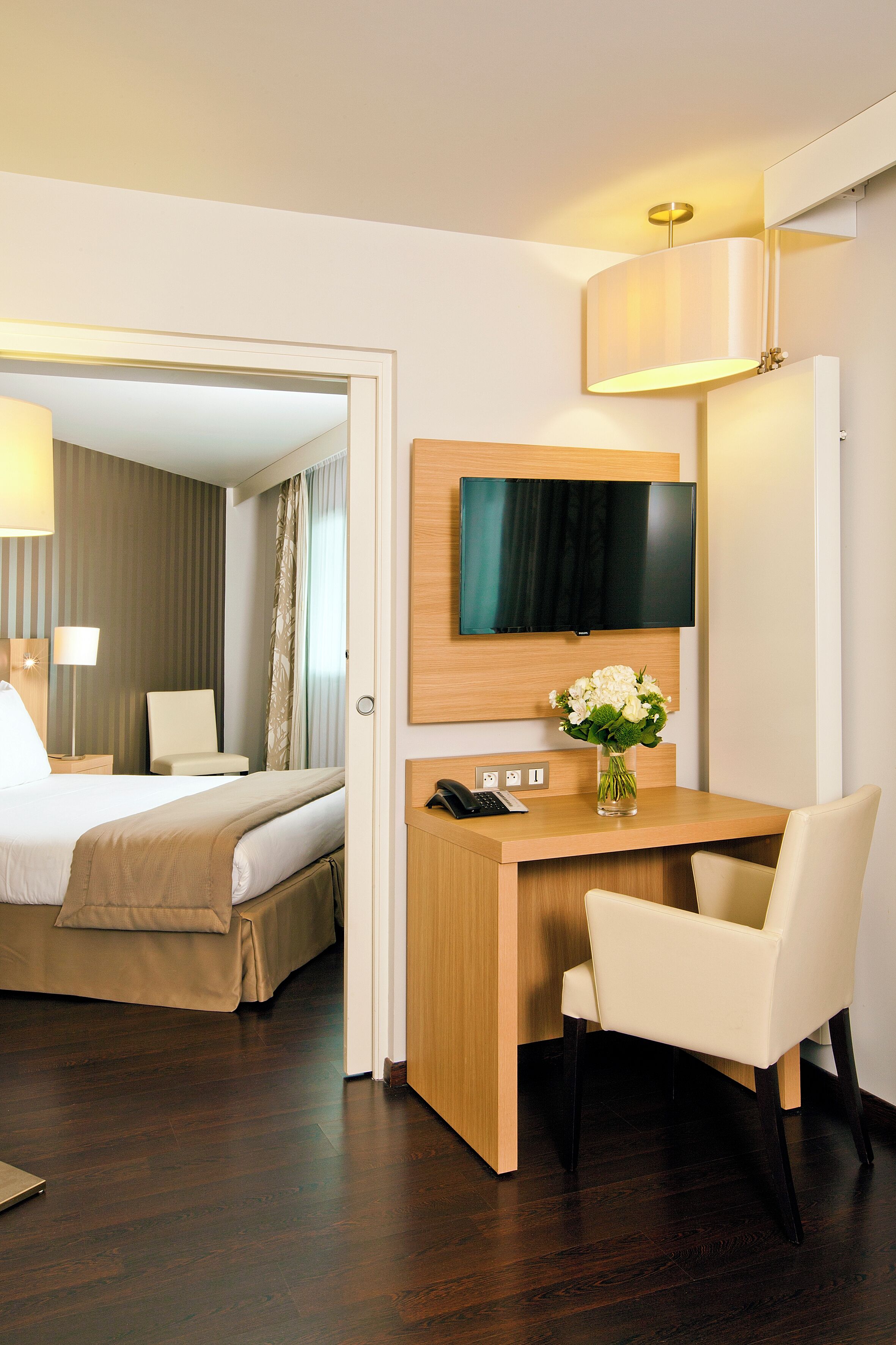 Une chambre d’hôtel avec un lit, un bureau et une chaise, une télévision et un vase avec des fleurs.