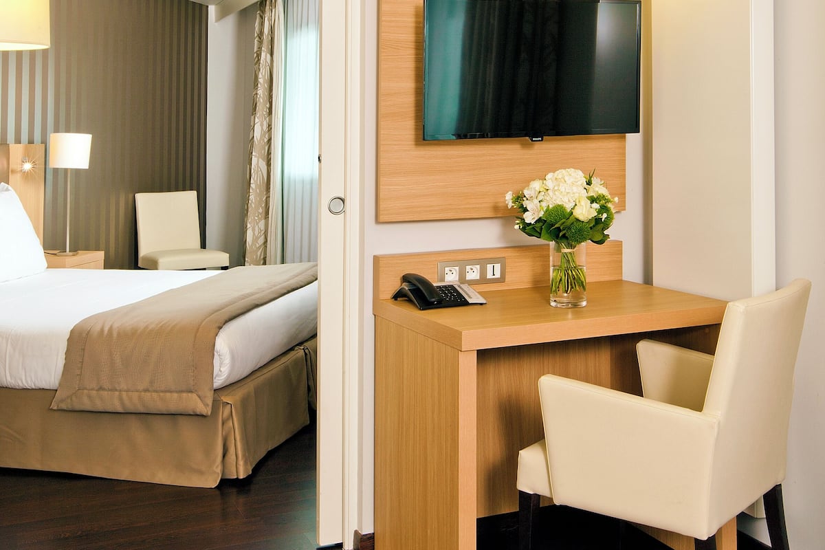 Une chambre d’hôtel avec un lit, un bureau et une chaise, une télévision et un vase avec des fleurs.