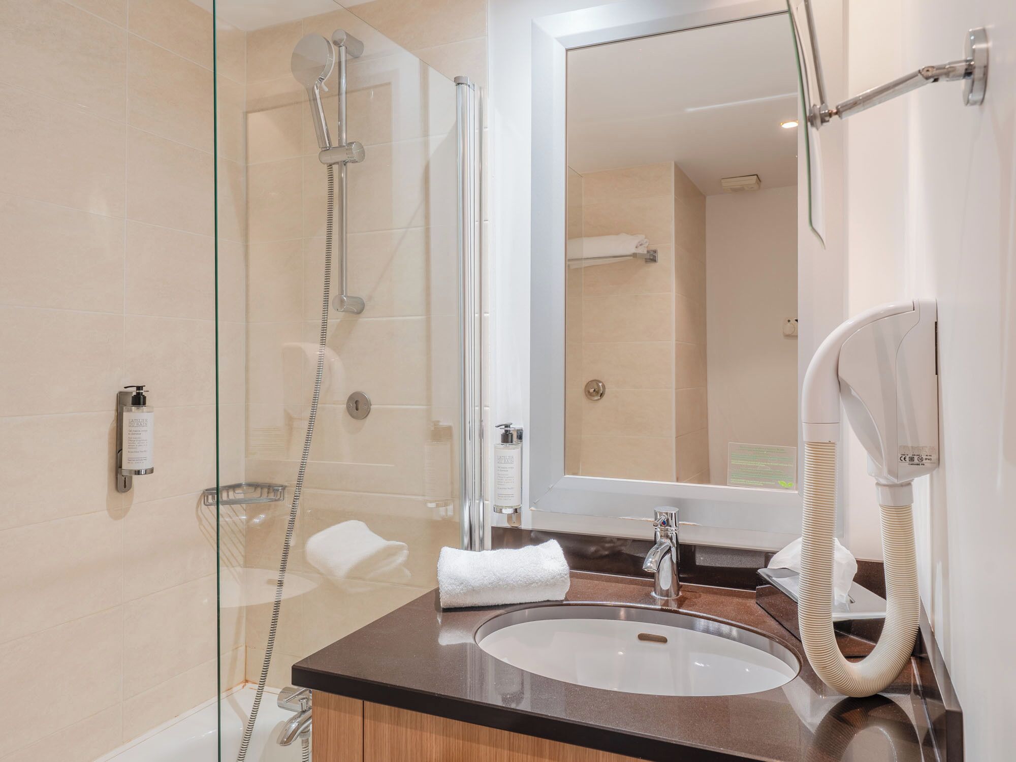A modern bathroom with a glass-enclosed shower, a sink, a mirror, and a hairdryer mounted on the wall.