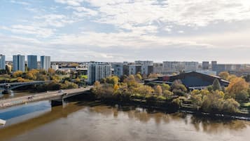 A riverside cityscape with modern buildings, a bridge, and autumn foliage.