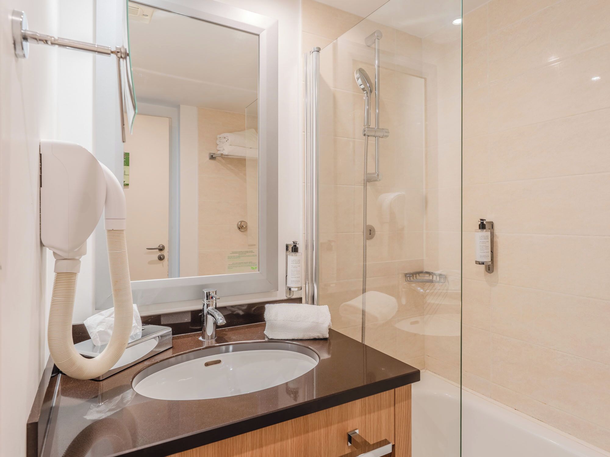 A modern bathroom with a glass-enclosed shower, a sink with a towel rack, and a hairdryer.
