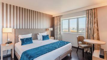 A hotel room with a large bed, a desk, a chair, and a view of the city through the window.