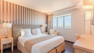 A hotel room with a large bed, two bedside tables, a desk, and a window with a city view.