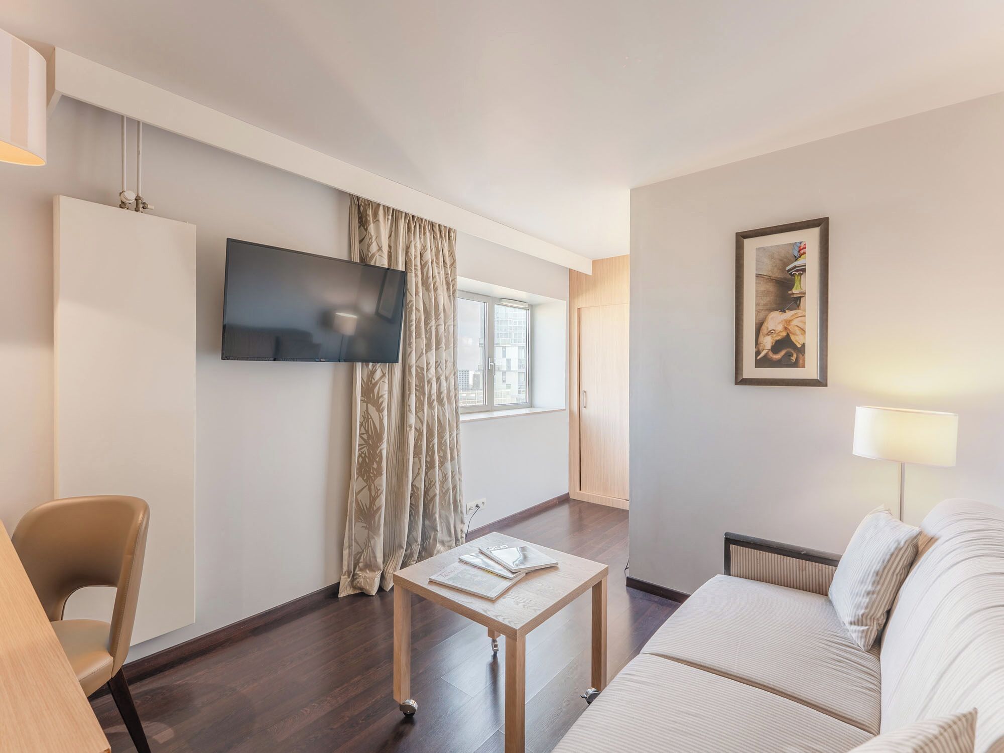 Una habitación de hotel moderna con una televisión de pantalla plana, un sofá, una mesa y un ventanal con cortinas.
