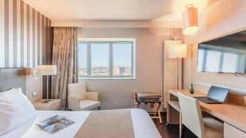 A hotel room with a bed, a desk, a chair, a TV, and a window with a city view.
