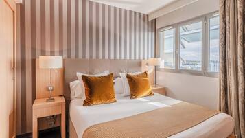 Quarto de hotel com uma cama grande, duas mesas de cabeceira, uma janela com cortinas e uma parede listrada.