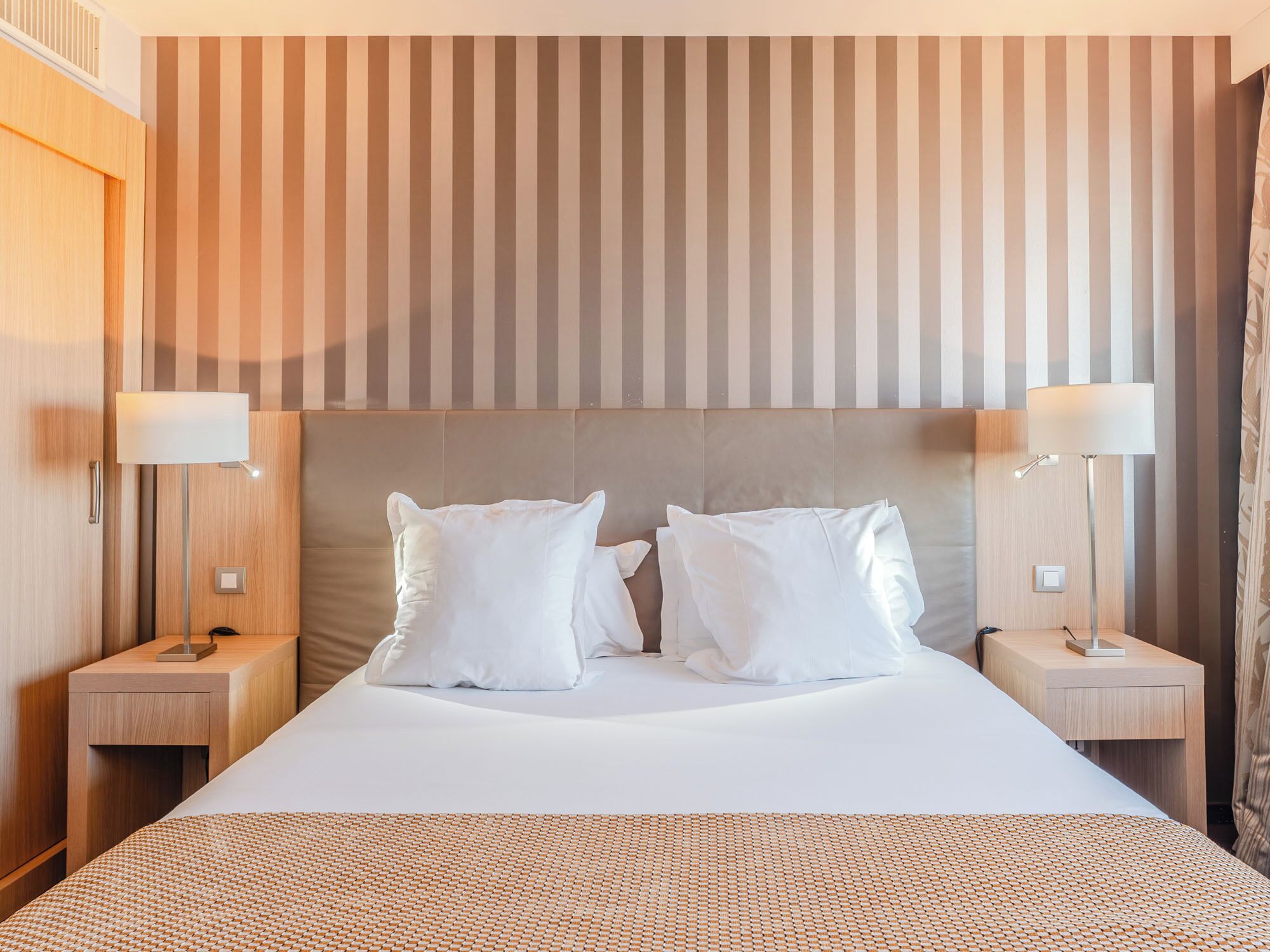A hotel room with a large bed, two bedside tables, and a striped wall.