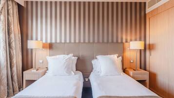 Habitación de hotel con dos camas, cabecera a rayas, lámparas de noche y un armario de madera.